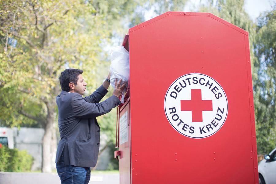 Mann spendet Kleidung in einen roten DRK-Sammelcontainer für Kleiderspenden im Freien.
