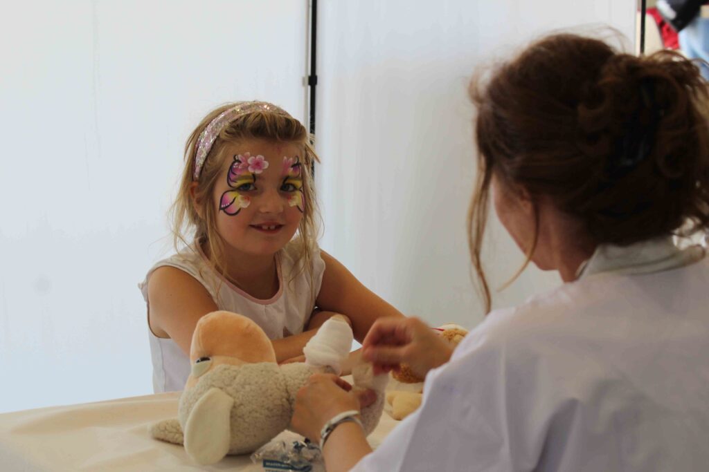 Kleines Mädchen mit Gesichtsschminke behandelt ein Kuscheltier in der Teddyklinik beim DRK-Familientag