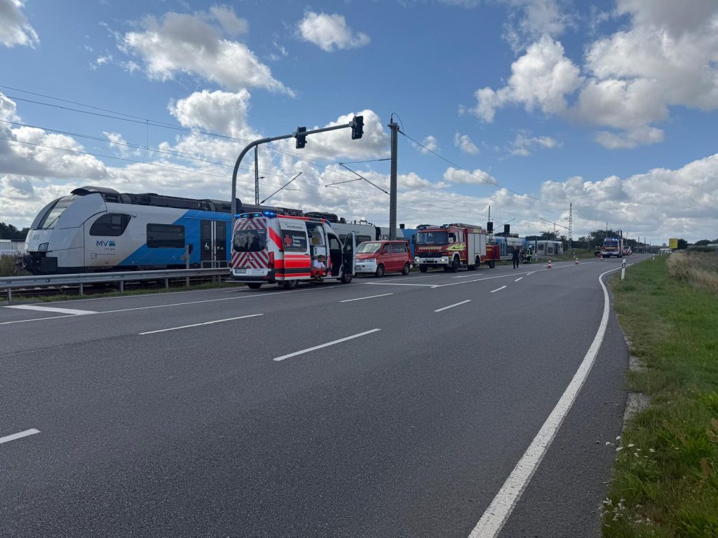 Einsatzfahrzeuge von Feuerwehr und Rettungsdienst an einem Bahnübergang neben einem Regionalzug